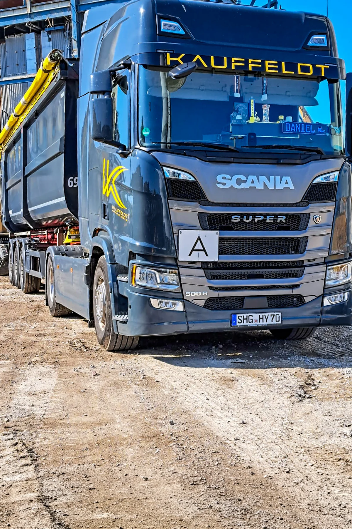 Schüttguttransporter der Firma Kauffeldt auf sandigem Untergrund vor einer Bauruine.
